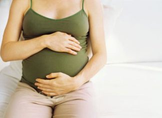 Woman sits on bed, holding pregnant belly.