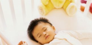 Sleeping baby with spikey black hair in a crib.