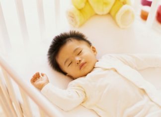 Sleeping baby with spikey black hair in a crib.