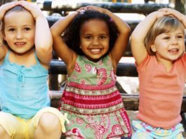 Close-up of three girls sitting and smiling with their hands on their heads.