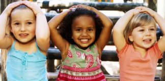 Close-up of three girls sitting and smiling with their hands on their heads.