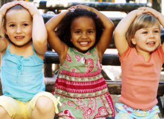 Close-up of three girls sitting and smiling with their hands on their heads.