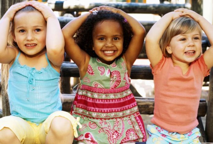 Close-up of three girls sitting and smiling with their hands on their heads.
