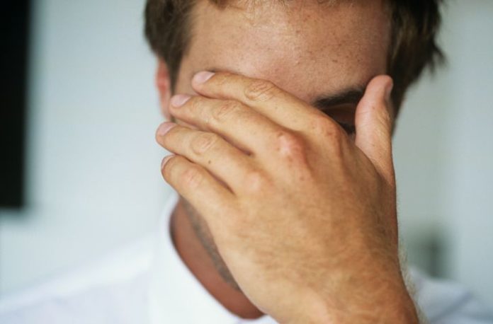 A man hides his face with his left hand.