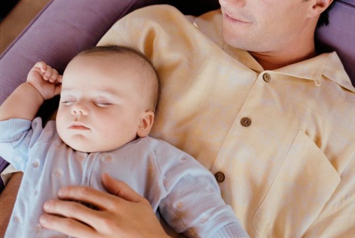 Father holds baby. Both rest.