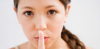 A girl with a long braid holds her pointer finger over her lips, miming the "shhhh" action.
