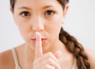 A girl with a long braid holds her pointer finger over her lips, miming the "shhhh" action.