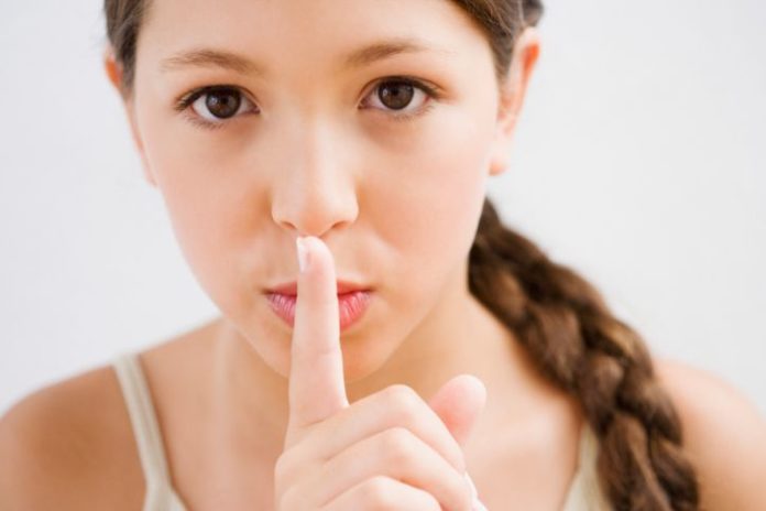 A girl with a long braid holds her pointer finger over her lips, miming the 