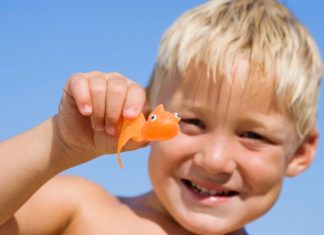 Blond boy in the sun with toy orange fish.