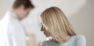 A depressed looking scene as a woman looks over her shoulder the the doctor in the background. He is out of focus.