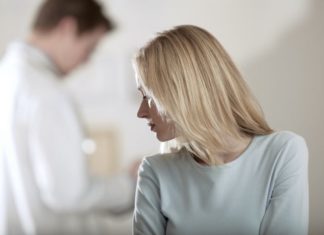 A depressed looking scene as a woman looks over her shoulder the the doctor in the background. He is out of focus.