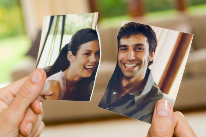 A woman's hands hold a torn photo of a couple