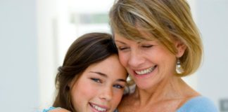 A mother holds her teen daughter around the shoulders.