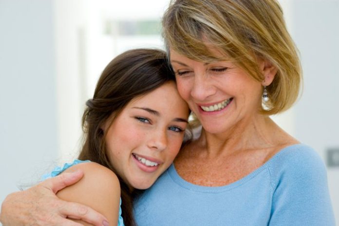 A mother holds her teen daughter around the shoulders.