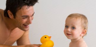 Father and son enjoying bath time. Father shows the baby a rubber ducky.