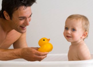 Father and son enjoying bath time. Father shows the baby a rubber ducky.