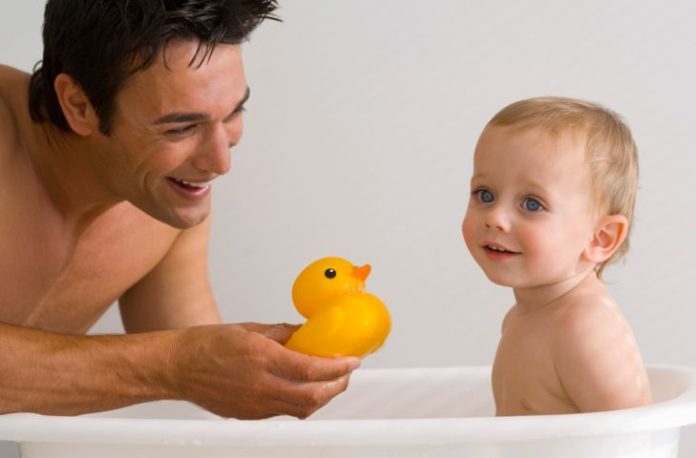 Father and son enjoying bath time. Father shows the baby a rubber ducky.