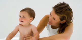 Mother stands her baby up in the tub.