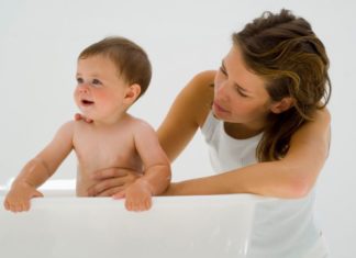 Mother stands her baby up in the tub.