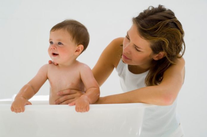 Mother stands her baby up in the tub.