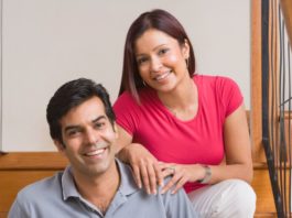 A happy couple pose on a stair case. They are sitting down.