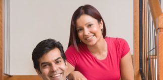 A happy couple pose on a stair case. They are sitting down.