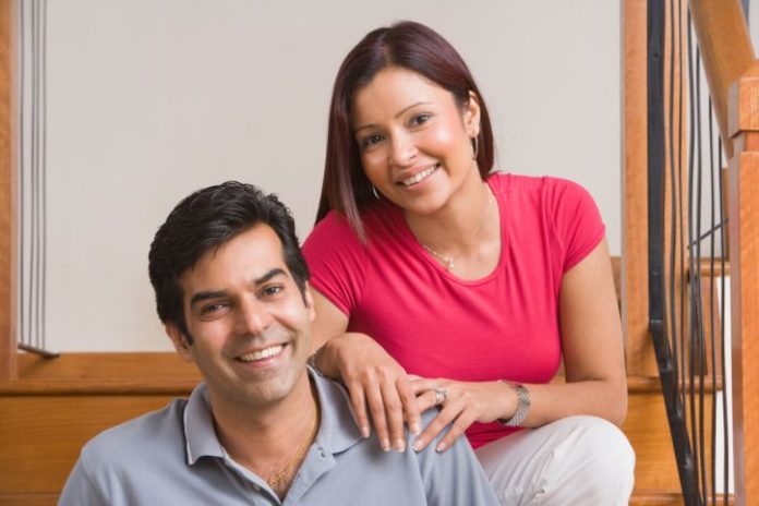 A happy couple pose on a stair case. They are sitting down.