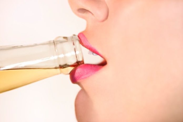 Close up of a woman drinking alcohol from a bottle.