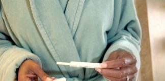 Woman in bathrobe holds a pregnancy test.