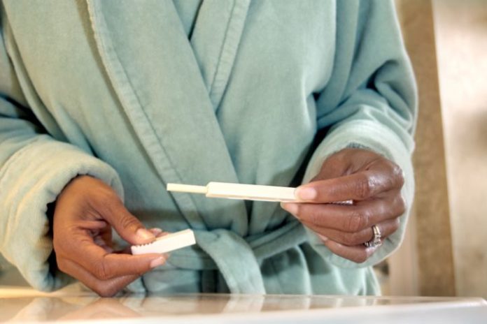 Woman in bathrobe holds a pregnancy test.