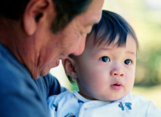 Grandfather smiles on as little boy looks out.