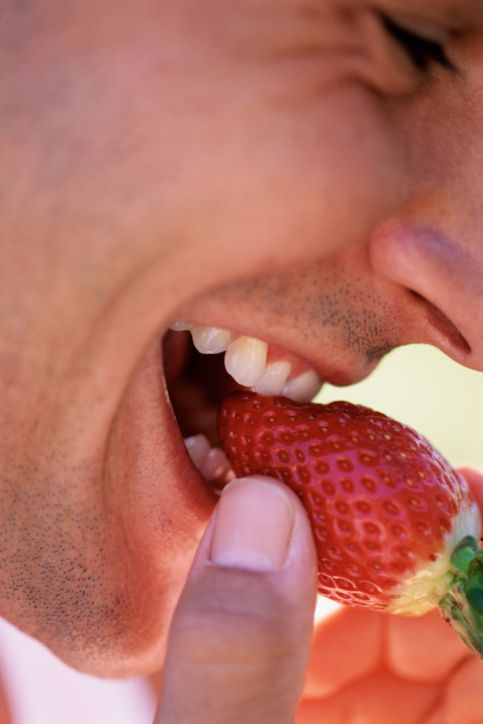 Close up of man's teeth as he bites into a strawberry. His teeth are perfect.