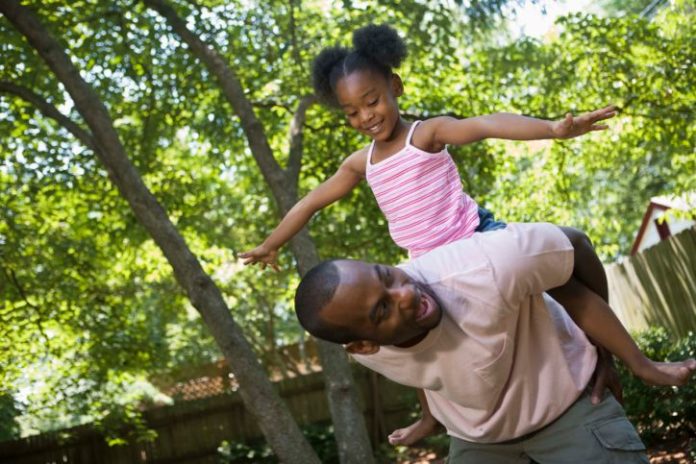 Father and daughter playing outside. The girl is on her father's back.