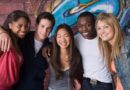 A group of teenagers smiling in front of a wall with graffiti on it.