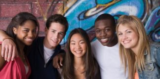 A group of teenagers smiling in front of a wall with graffiti on it.