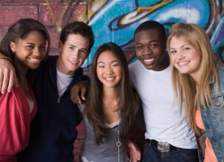 A group of teenagers smiling in front of a wall with graffiti on it.