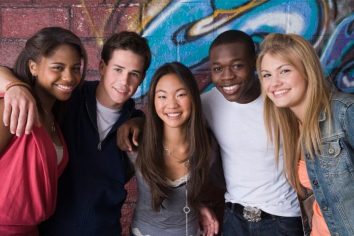 A group of teenagers smiling in front of a wall with graffiti on it.