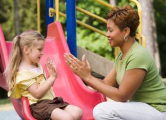 A woman playing hand games with girl at playground.