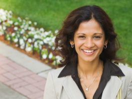 A woman in business attire stands on a cement path in front of a row of flowers.