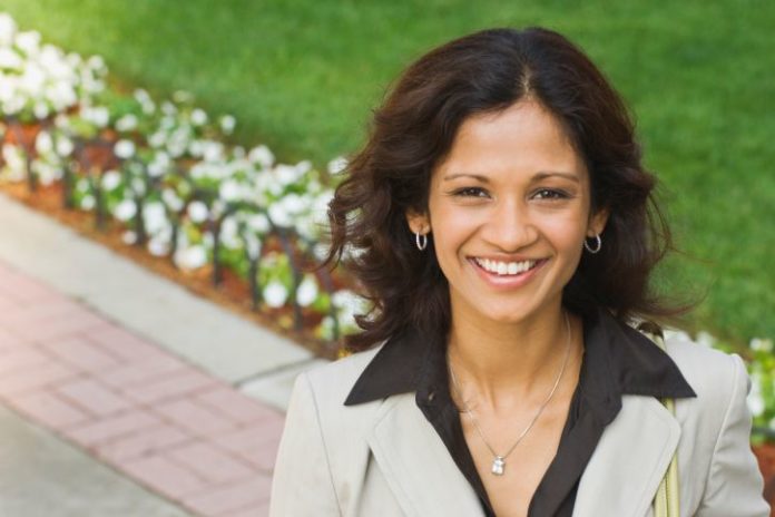 A woman in business attire stands on a cement path in front of a row of flowers.