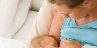 A mother and baby lay in bed while the baby feeds.