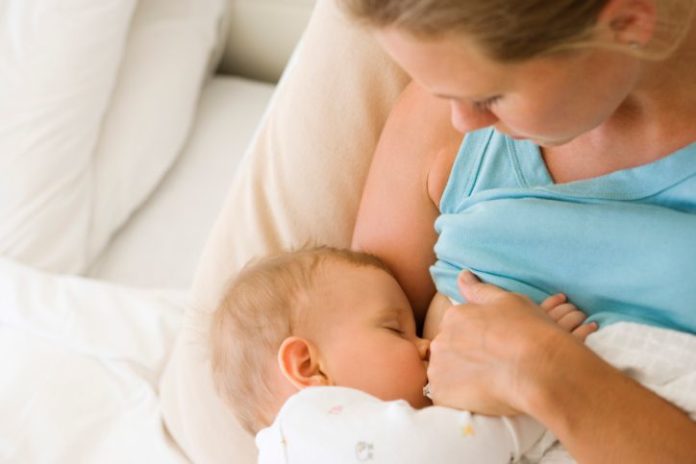 A mother and baby lay in bed while the baby feeds.