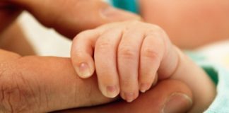 A newborn's hand is held in the palm of a man's hand.