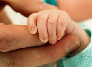 A newborn's hand is held in the palm of a man's hand.