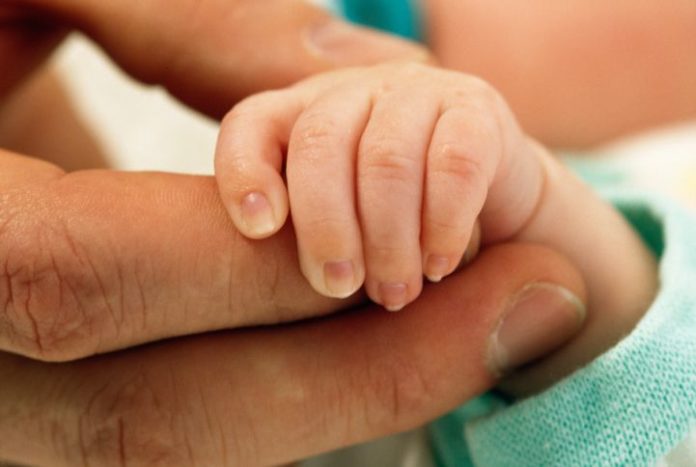 A newborn's hand is held in the palm of a man's hand.