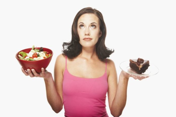 Woman balancing food. In one hand is a salad and in the other, a large piece of chocolate cake.