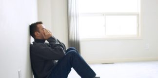 Upset man leaning against a wall with his hands over his eyes and face.