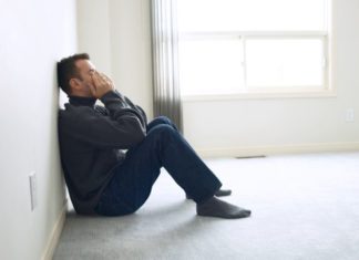 Upset man leaning against a wall with his hands over his eyes and face.