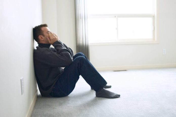 Upset man leaning against a wall with his hands over his eyes and face.