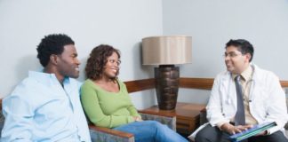 A couple consult with a doctor in what looks to be a waiting room. Everyone is smiling.